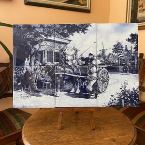 May include: A blue and white tile mural depicting a rural scene with a horse-drawn carriage, a windmill, and figures in traditional attire. The mural is displayed on a wooden easel, showcasing a detailed illustration of a village.