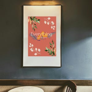 Könnte beinhalten: Gerahmter Kunstdruck mit dem Schriftzug "Everything has its time" auf korallenfarbenem Hintergrund. Der Druck zeigt botanische Elemente im Aquarellstil in Grün, Weiß und Gelb. Das Kunstwerk wird an einer dunkelgrauen Wand über einem kleinen Tisch und Stuhl ausgestellt.