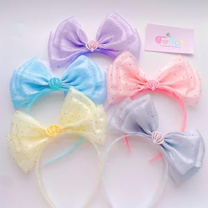 Peut inclure: Cinq serre-têtes ornés de grands nœuds transparents à pois dans les tons lavande, bleu clair, jaune pâle, rose tendre et pervenche. Chaque nœud est centré par une petite breloque coquillage en plastique. Une carte avec le texte Let's Cute est incluse.