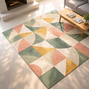 May include: A large area rug with a geometric pattern in shades of green, yellow, pink, and cream. The rug features a mix of triangles and curved shapes, creating a modern and colorful design. The rug is placed in a living room setting.