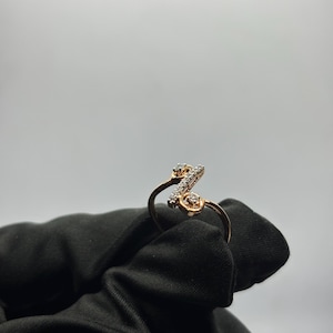 Puede incluir: Un anillo de oro rosa con un dise&ntilde;o de letra "Z" en cursiva, incrustado con peque&ntilde;os diamantes brillantes. El anillo se presenta sobre un fondo blanco liso, resaltando los detalles intrincados de la joya.