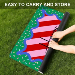 May include: A rolled-up black mat with a colorful design featuring a cake motif. The cake has red and pink stripes, a green border with sprinkles, and the words "Happy" and "XOXO" in black. The text "EASY TO CARRY AND STORE" is at the top.