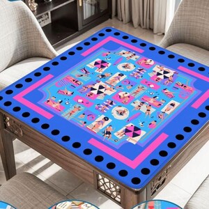 May include: A square wooden table with a blue top featuring a pink and blue beach scene design. The table has a dark wood frame and is surrounded by light gray chairs. The table's top has a border of black circles.