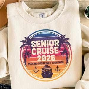 Könnte beinhalten: Cremefarbenes Sweatshirt mit farbenfroher Grafik. Die Grafik zeigt die weißen Worte "SENIOR CRUISE 2026" mit Palmen, einem Kreuzfahrtschiff und Ankern. Der Satz "MAKING MEMORIES TOGETHER" ist ebenfalls enthalten.