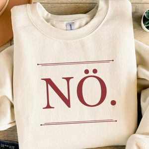 Könnte beinhalten: Set aus drei Keramikbechern mit gesprenkelter, matter Oberfläche. Die Becher sind in Creme-, Hellgrau- und Dunkelgrautönen gehalten. Jede Tasse hat ein schlichtes, minimalistisches Design.