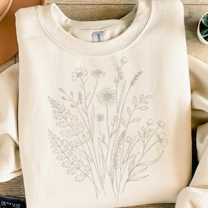 Könnte beinhalten: Cremefarbenes Sweatshirt mit detailliertem grauem Blumendesign. Das Design umfasst verschiedene Blumen und Blätter, wodurch eine botanische Illustration entsteht. Das Sweatshirt hat einen Rundhalsausschnitt und lange Ärmel und bietet einen lässigen und bequemen Stil.