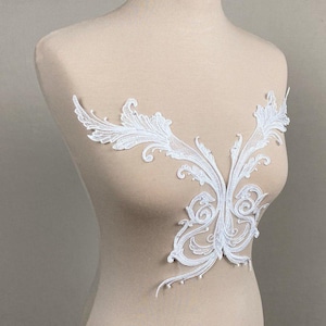 May include: A white lace applique featuring an intricate symmetrical scrollwork design with delicate floral-inspired patterns. The embroidery is crafted with fine thread detailing, creating a decorative piece for garment embellishment.