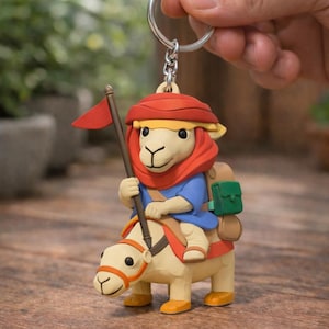 Peut inclure: Porte-clés fantaisiste représentant un chameau avec un cavalier. Le chameau est beige clair avec des détails orange, portant un drapeau rouge. Le cavalier porte un chapeau rouge, une chemise bleue et un sac à dos vert. Le porte-clés est fixé à un anneau argenté.
