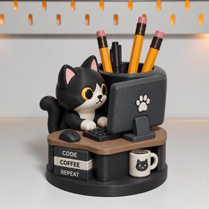 May include: A black and white cat figurine desk organizer featuring a computer monitor with a paw print, a keyboard, and a mouse. The base includes three stacked books labeled CODE, COFFEE, REPEAT, and a small white mug with a cat face illustration.