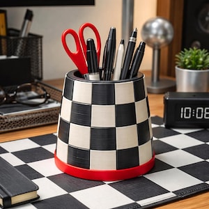 May include: A black and white checkered pen holder with a red base, holding red scissors, pens, and a pencil. The desk accessory sits on a black and white checkered surface, with a digital clock displaying 10:08 in the background.