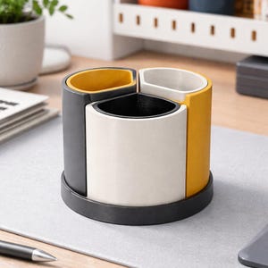 May include: A desk tidy with a circular design, featuring three compartments in grey, white, and yellow. Each section has a black interior. The tidy sits on a dark grey base. Ideal for organising pens and stationery.