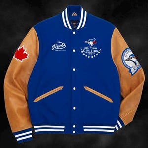 May include: A blue and tan varsity jacket with white stripes on the collar, cuffs, and hem. The jacket features a maple leaf patch, team logos, and the text "Roots". The sleeves are tan, and the body is blue. The jacket has a button-up front.