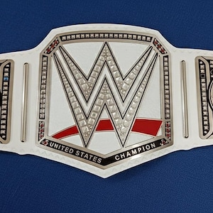 May include: A white and silver WWE United States Championship belt. The belt features the WWE logo in the center, with the words "UNITED STATES CHAMPION" below. The belt has a red stripe and blue accents.