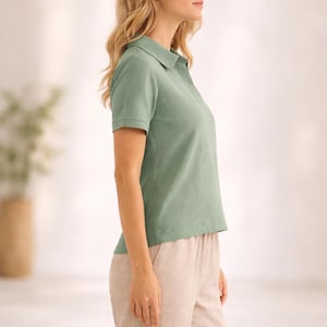 May include: A sage green short-sleeved polo shirt with a classic collar and a buttoned placket, paired with light beige trousers. The shirt features a textured fabric finish and ribbed sleeve cuffs, providing a clean and simple look for daily wear.