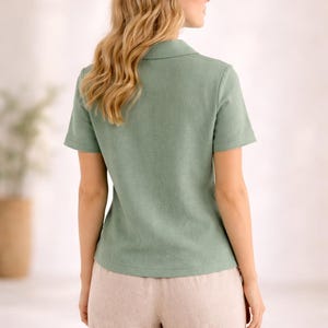 May include: A sage green short-sleeved shirt with a classic collar and a textured fabric finish, paired with light beige trousers. The shirt features a straight hemline and a simple button-down front design, providing a clean and structured appearance.