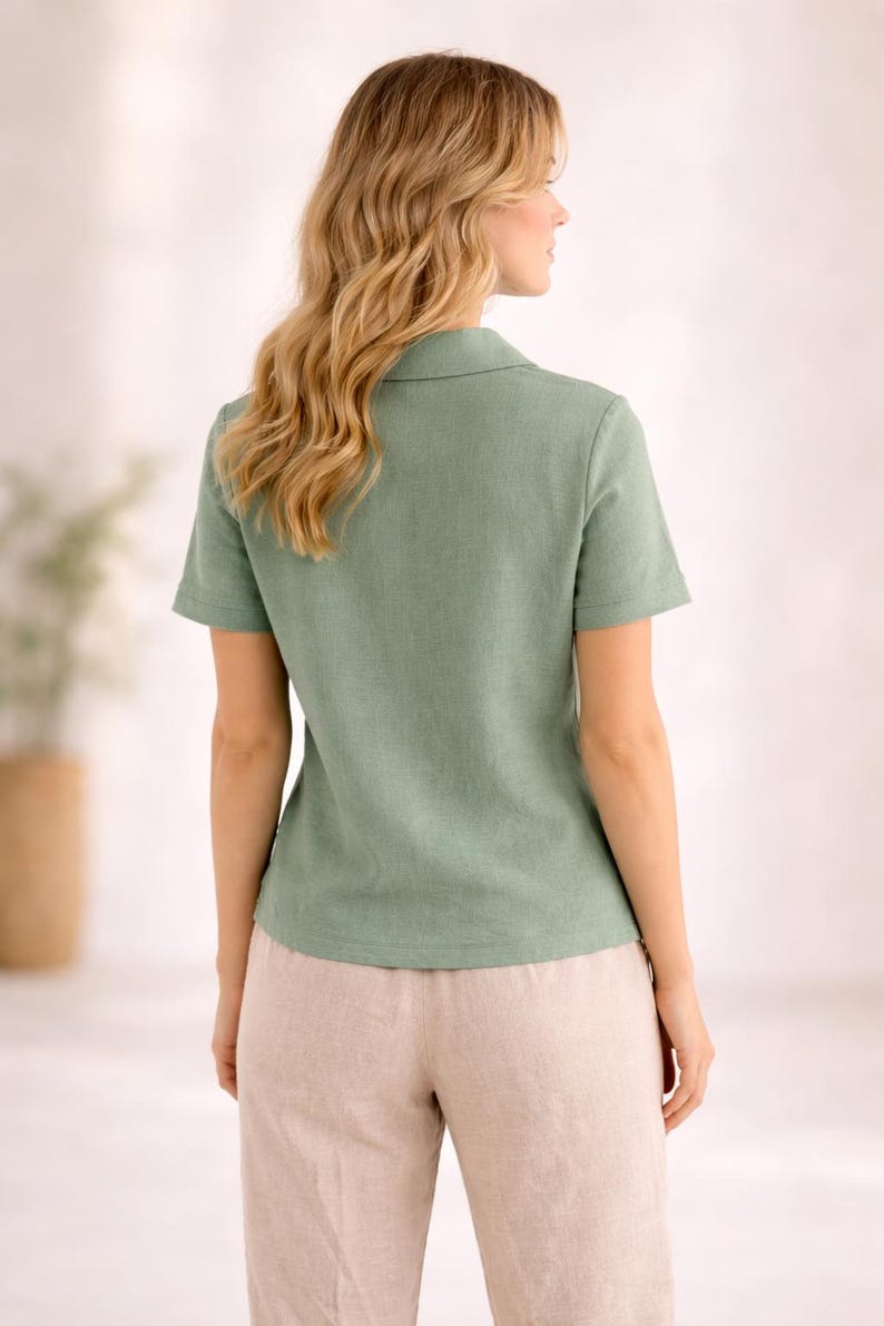 May include: A sage green short-sleeved shirt with a classic collar and a textured fabric finish, paired with light beige trousers. The shirt features a straight hemline and a simple button-down front design, providing a clean and structured appearance.