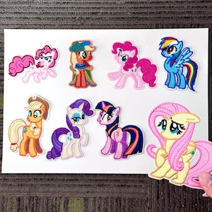 Puede incluir: Un conjunto de parches bordados coloridos con varios personajes de dibujos animados de ponis. Los parches muestran una gama de colores, incluyendo rosa, azul, amarillo, naranja y morado. Cada parche tiene costuras detalladas y diseños únicos.
