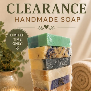 May include: A vertical stack of ten rectangular bars of handmade soap wrapped in clear plastic. The bars feature various colors including green, yellow, black, white, purple, and brown, with visible botanical inclusions and textured surfaces.