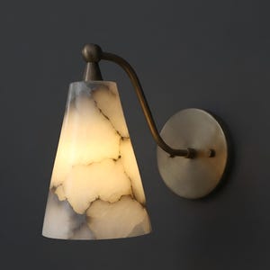 Può includere: Applique da parete con paralume conico bianco sporco con venature grigie. Il paralume è illuminato e l'apparecchio ha un braccio curvo color ottone e una piastra a muro circolare. Design moderno ed elegante.