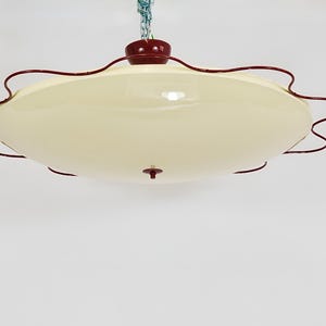 May include: A vintage-style ceiling light fixture with a cream-colored, oval-shaped shade. The fixture has a dark red trim and a matching top piece. A chain suspends the light from the ceiling.