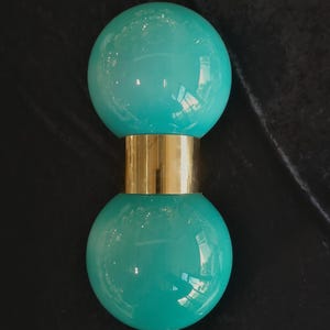 May include: A teal-colored, spherical lamp with a gold-colored band in the middle. The lamp has a glossy finish and a modern design. The lamp is a decorative lighting fixture.