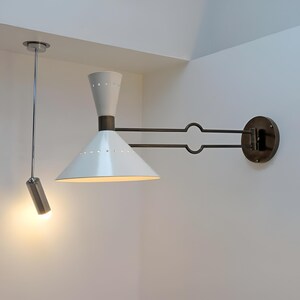 May include: A white and bronze wall-mounted lamp with a conical shade and a cylindrical ceiling-mounted spotlight. The wall lamp has a bronze arm and a circular base. The ceiling light is suspended by a thin metal rod.