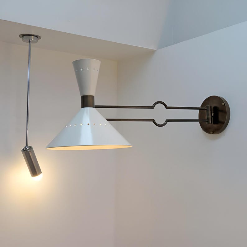 May include: A white and bronze wall-mounted lamp with a conical shade and a cylindrical ceiling-mounted spotlight. The wall lamp has a bronze arm and a circular base. The ceiling light is suspended by a thin metal rod.