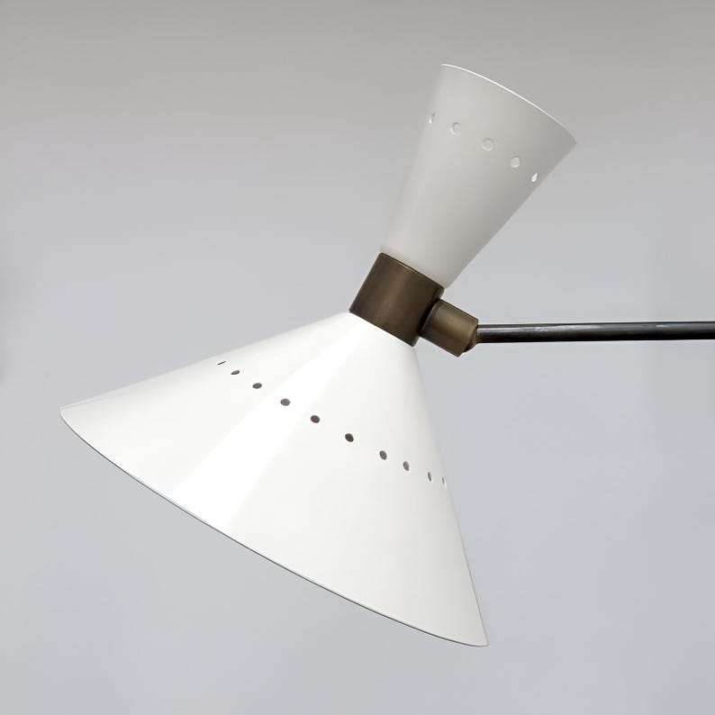 May include: A white, cone-shaped lamp with a brass-colored joint and a black arm. The lamp has small holes around the edge of the shade. The lamp is angled, with the light facing upwards. The lamp is a modern design.