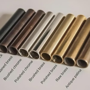 May include: An assortment of metal tubes in various finishes, including matte black, antique black, and polished brass. The tubes are arranged in a row, showcasing different textures and colors, with labels identifying each finish.