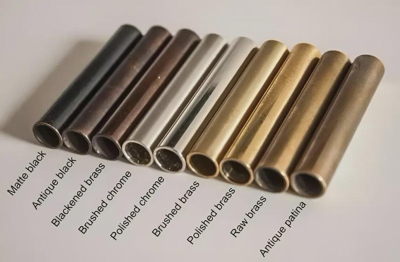 May include: An assortment of metal tubes in various finishes, including matte black, antique black, and polished brass. The tubes are arranged in a row, showcasing different textures and colors, with labels identifying each finish.