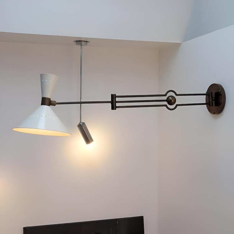 May include: A modern wall-mounted lamp with a white conical shade and a smaller cylindrical light. The lamp features a dark metal arm and a circular wall mount. The design is minimalist and stylish, suitable for interior lighting.