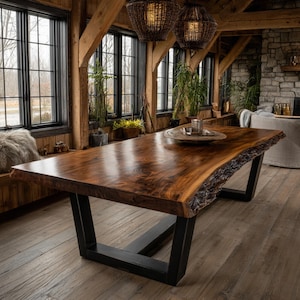Op de afbeelding: Een grote rechthoekige eettafel met een gepolijst bruin houten blad met een natuurlijke boomstamrand en een opvallende houtnerf. De tafel wordt ondersteund door twee stevige, zwarte metalen trapeziumvormige poten aan beide uiteinden.