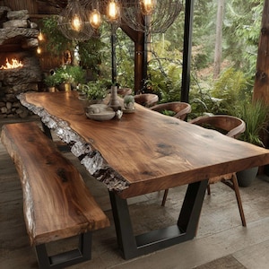 May include: A large live edge wooden dining table with a natural bark finish on the sides and a smooth brown surface, supported by black metal legs. A matching wooden bench sits alongside, accompanied by several curved wooden chairs.
