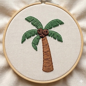 May include: Hand-stitched embroidery art featuring a palm tree design. The artwork showcases a brown trunk, green fronds, and brown coconuts, all set against a neutral fabric background. The embroidery is framed in a wooden hoop, perfect for wall decor.