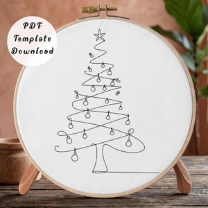 Op de afbeelding: Een ronde houten borduurring met witte stof waarop een zwarte lijntekening van een kerstboom met kleine ornamenten en een ster aan de top staat. De tekst PDF Template Download is linksboven op de afbeelding gedrukt.
