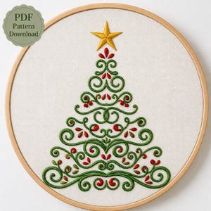 May include: A circular wooden embroidery hoop containing a white fabric panel with a hand-stitched Christmas tree design. The tree is formed by green swirling scrollwork, red embroidered accents, and a single yellow star at the top.