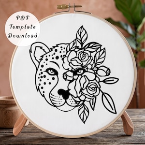 May include: A round wooden embroidery hoop containing white fabric with a black line art design. The design features a leopard head on the left side and a cluster of roses with leaves on the right side. A circular white label reads PDF Template Download.