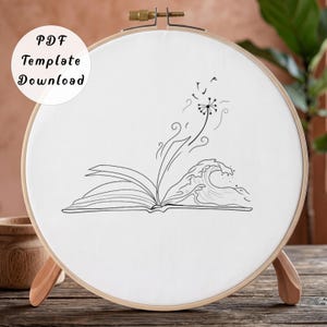 May include: A circular wooden embroidery hoop containing white fabric with a black line art illustration of an open book. From the pages, a wave rises and a dandelion releases seeds into the air. The text PDF Template Download is visible.