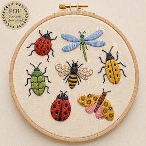 Puede incluir: Un bastidor de bordado redondo de madera que contiene un panel de tela color crema con insectos bordados a mano. El diseño presenta dos mariquitas rojas, una libélula azul, un escarabajo verde, una abeja amarilla y negra, un escarabajo amarillo y una polilla con alas rosas y amarillas.