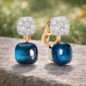 Puede incluir: Un par de pendientes de clip con una sección superior cuadrada pavimentada con pequeñas piedras claras en un engaste plateado, conectada a una piedra translúcida de color azul profundo y talla cojín. Los componentes metálicos son dorados.