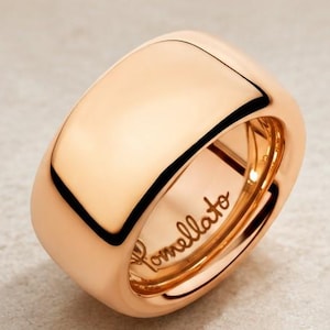Könnte beinhalten: Ein breiter, polierter Ring aus Roségold mit einer glatten, abgerundeten Außenfläche. Die Innenseite des Rings ist mit dem eingravierten Schriftzug Pomellato versehen und weist eine hochglänzende Metalloberfläche sowie ein massives Profil auf.