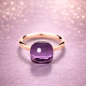 Può includere: Un anello d'oro con una grande pietra preziosa viola a taglio quadrato. L'anello ha una fascia semplice e lucida e un'incastonatura a castone. Lo sfondo è rosa sfocato con bokeh.
