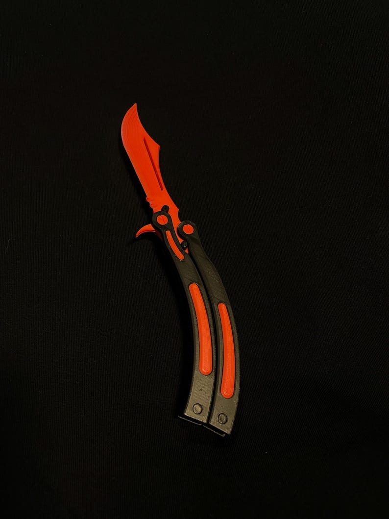May include: A butterfly knife with a bright red blade and accents. The handle is black with red stripes. The knife is shown against a black background.