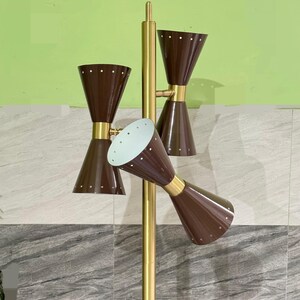 May include: A floor lamp featuring a central gold-toned metal pole with three adjustable, double-cone shaped shades in a dark brown finish. Each shade is accented with a series of small, evenly spaced white dots along the top and bottom rims.