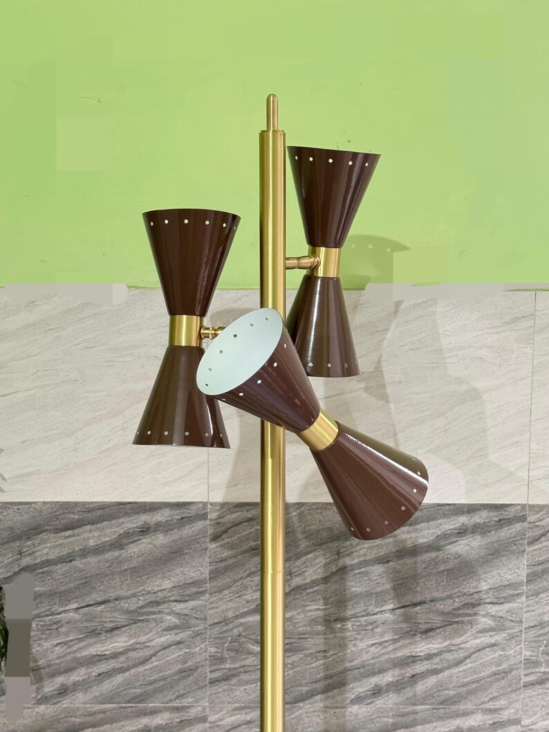 May include: A floor lamp featuring a central gold-toned metal pole with three adjustable, double-cone shaped shades in a dark brown finish. Each shade is accented with a series of small, evenly spaced white dots along the top and bottom rims.