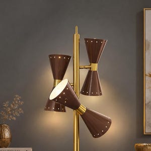 May include: A floor lamp featuring a central gold-toned metal pole with three double-cone shaped shades in a dark brown finish. Each cone shade is accented with a series of small circular perforations along the edges, emitting a warm light.
