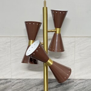 May include: A floor lamp featuring a central gold-toned metal pole with three brown, hourglass-shaped shades. Each shade is accented with small white dots along the rims and has a white interior. The lamp structure is made of gold-colored metal.