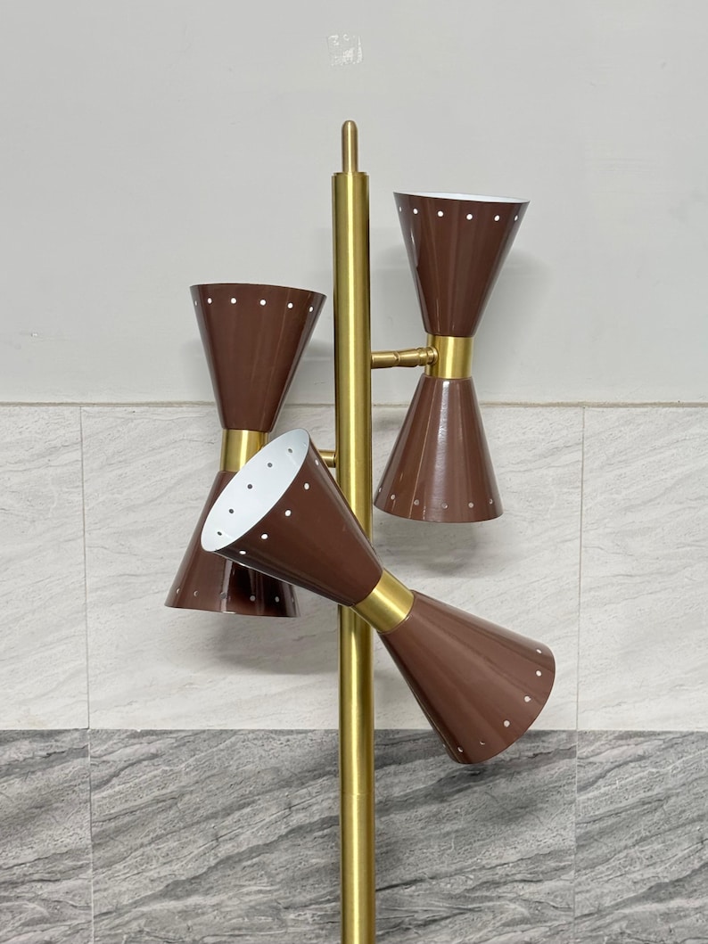 May include: A floor lamp featuring a central gold-toned metal pole with three brown, hourglass-shaped shades. Each shade is accented with small white dots along the rims and has a white interior. The lamp structure is made of gold-colored metal.