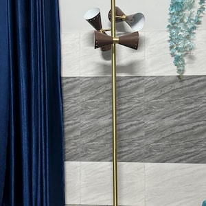 May include: A floor lamp with a tall, slender gold-toned metal pole and a circular white marble base. It features three adjustable brown cone-shaped shades with white interiors and small perforated holes, mounted on a central gold-toned fixture.