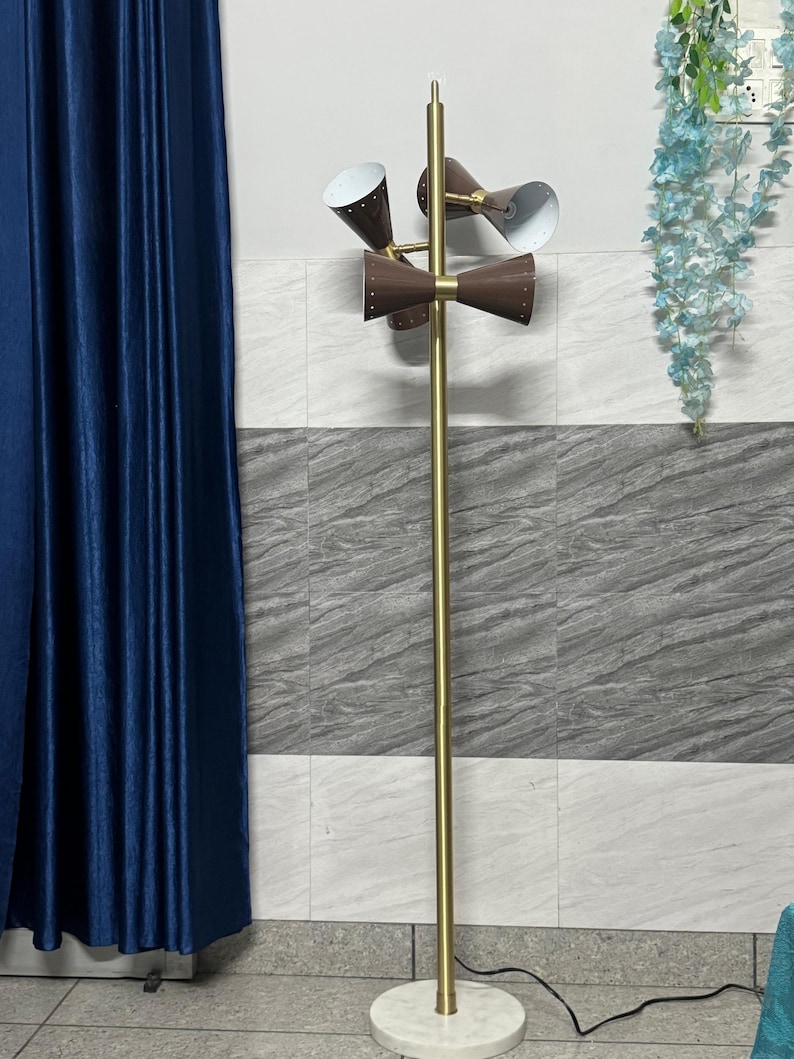 May include: A floor lamp with a tall, slender gold-toned metal pole and a circular white marble base. It features three adjustable brown cone-shaped shades with white interiors and small perforated holes, mounted on a central gold-toned fixture.
